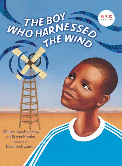A young boy looks up to a windmill turning in the wind behind him.